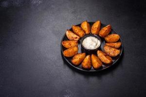 Baked potato wedges with cheese and herbs and tomato sauce on a dark background photo