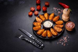 Baked potato wedges with cheese and herbs and tomato sauce on a dark background photo