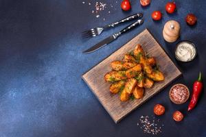 Baked potato wedges with cheese and herbs and tomato sauce on a dark background photo