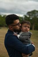 padre pakistaní asiático sostiene a su bebé de 11 meses en el parque local foto