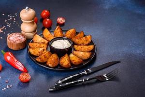 Baked potato wedges with cheese and herbs and tomato sauce on a dark background photo