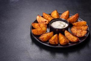 Baked potato wedges with cheese and herbs and tomato sauce on a dark background photo