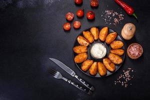 Baked potato wedges with cheese and herbs and tomato sauce on a dark background photo