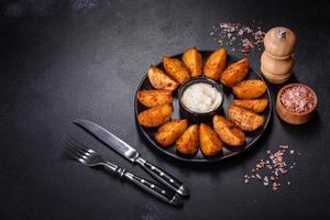 Baked potato wedges with cheese and herbs and tomato sauce on a dark background photo