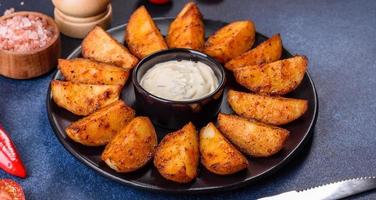 Baked potato wedges with cheese and herbs and tomato sauce on a dark background photo