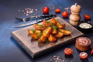 Baked potato wedges with cheese and herbs and tomato sauce on a dark background photo