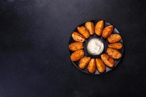 Baked potato wedges with cheese and herbs and tomato sauce on a dark background photo