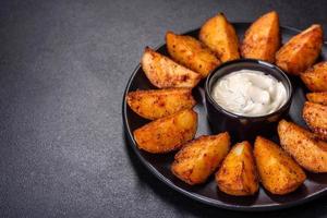 Baked potato wedges with cheese and herbs and tomato sauce on a dark background photo