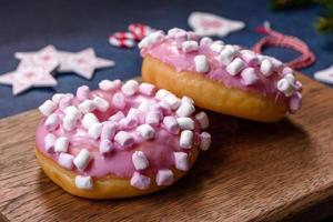 Pink glazed doughnut and marshmallow with Christmas decorations on a wooden cutting board photo