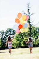 Two little girls holding a bunch of balloons together. photo