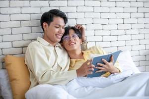 Gay couple reading book together on bed at home,  LGBTQ concept. photo