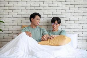 Happy asian gay couple holding hands together relaxing at home on bed, LGBTQ concept. photo