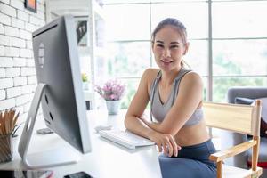 joven mujer asiática que usa una computadora portátil revisando la aplicación de medios sociales en el sitio web en línea en casa, siéntase relajada y disfrute comunicándose y discutiendo en la sala de estar. foto