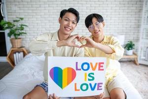 Asian gay couple holding lgbt rainbow sign at home,  LGBTQ concept. photo
