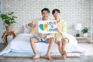 pareja gay asiática con cartel de arco iris lgbt en casa, concepto lgbtq. foto