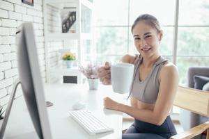 Young Asian woman using laptop computer checking social media application on website online with coffee at home, feel relax and enjoy communicate and discuss  in living room.
