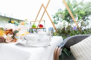 Coffee cup and flowers bouquet on table in garden. Afternoon tea concept. Home outdoor furniture. Wicker chair and table with white tablecloth in vintage style. Cozy chair and table on the terrace.