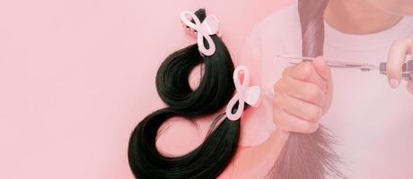 Hair donation for breast cancer person concept. Donate hair to wigs for breast cancer patients. Donate to cancer charity. Asian woman cutting long hair with scissors for donating on pink background. photo