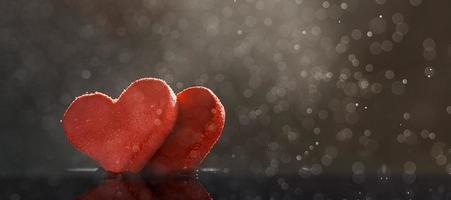 dos corazones rojos con gotas de lluvia iluminadas por una luz cálida sobre un fondo oscuro con un bokeh. foto con espacio de copia.