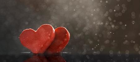 Two red hearts with rain drops illuminated by warm light on dark background with a bokeh. Photo with copy space.