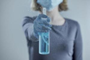 A girl in a medical mask blurs the transparent surface with a sanitizer. Photo with bokeh. Front view.