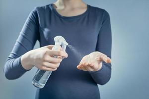 A girl treats her hands with sanitizer on gray background. Spray sanitizer on the background of a girl. photo