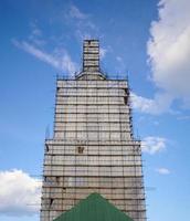 Scaffolding from planks around old bell tower. Background blue sky with clouds. photo