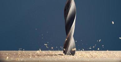 Metal wet drill bit make holes in wooden surface on industrial drilling machine with shavings on gray background. photo
