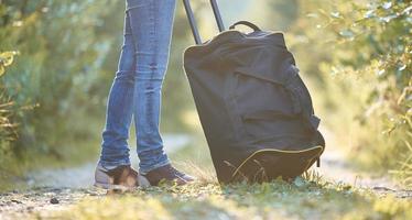 piernas de mujer y una bolsa de viaje negra en la carretera del pueblo. foto