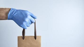 Hand in blue rubber gloves holds a paper bag. Photo with copy space. Concept of security during a pandemic.