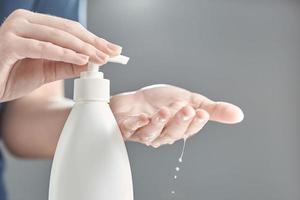 Female hands using hand sanitizer gel pump dispenser. Drops of gel close-up. photo