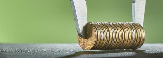 Calipers and stack of coins close-up against a green wall. photo