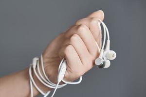 White headphones in his fist. The wire binds the hand. The concept of dependence on headphones. photo