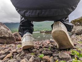 View between the feet of a crouching hiker on a water edge of Norway fjords photo