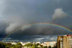 Rainbow over city. Atmospheric phenomenon in sky against background of thunderclouds.