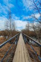 Old wooden bridge over the river in village. Narrow pedestrian crossing. Perspective. Spring nature outside the city. photo