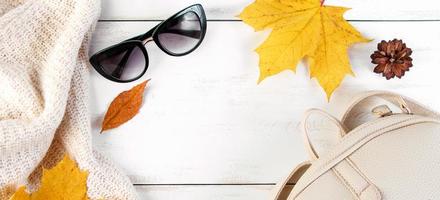 Hello autumn. Creative flat lay composition on white background. Yellow leaves, knitted sweater, backpack and glasses. photo