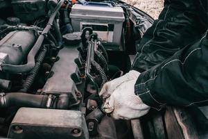 Replacing high-voltage wires on car engine. Man mechanic repairing an old vehicle is in service. Open hood auto photo