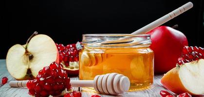 Rosh Hashanah celebration. Jar with honey, apples and pomegranates on dark wooden background. Jewish traditional religious holiday. Place for your text, banner format. photo