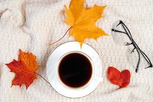 Cup of hot strong coffee and fallen leaf. Autumn morning concept. Warm beverage for cold weather and knitted sweater. photo