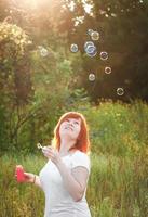 soñadora joven pelirroja con pompas de jabón. chica feliz en la naturaleza bajo el sol. un símbolo de libertad y disfrute. foto