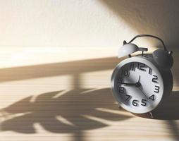 white vintage alarm clock on wooden table with morning sunlight and monstera leaf shadow. photo