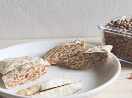 Raw tempeh or tempe. tempeh slices in white ceramic plate and bowl of dry soybean seeds  on wooden  table.  Tempeh is a traditional Indonesian food. photo