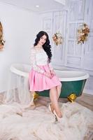 Young brunette girl in pink skirt and white blouse posed indoor against room with decor bath. photo