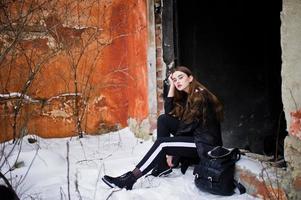 Fashionable long legs brunette model in long black cloak posed outdoor at winter day against old grunge wall. photo