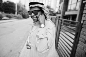 hombre de negocios árabe del medio oriente posó en la calle contra un edificio moderno con gafas de sol, hablando por teléfono móvil. foto