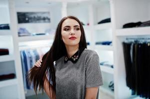 hermosa chica morena en la boutique de la tienda de ropa en vestido gris. foto