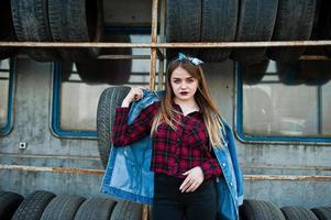 joven hipster con chaqueta de jeans y pañuelo en la cabeza en la zona de montaje de neumáticos. foto