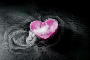 smoke of dry ice with pink heart shaped cup isolated on black background photo