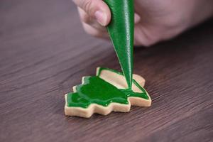 primer plano de dibujo de galletas de azúcar de árbol de Navidad sobre fondo de mesa de madera con glaseado. foto